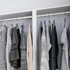Close up of white closet with nickel oval rods and hanging clothes