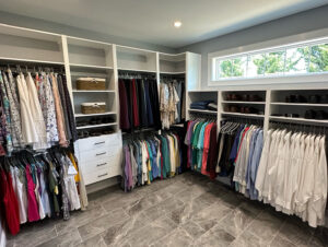Image of corner in a walk-in closet. The closet contains drawers, shelves and women's and men's hanging clothing.